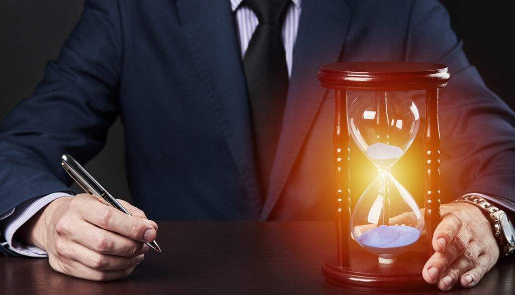 businessman holding pen at his arm and hourglass